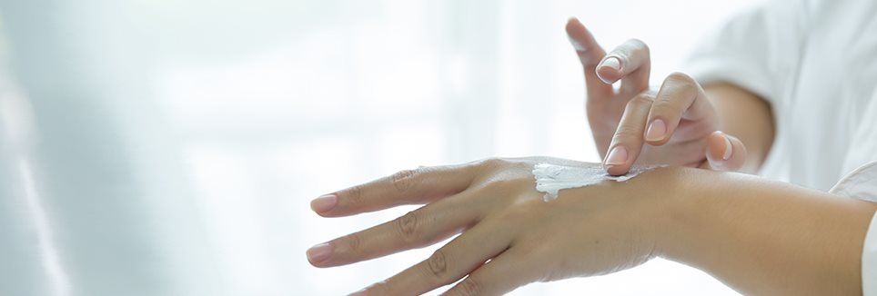 Jemand mit Neurodermitis an der Hand cremt die Hände ein