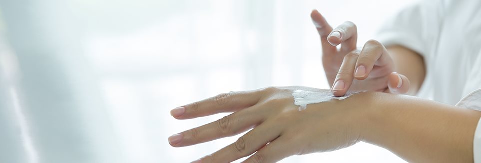 Jemand mit Neurodermitis an der Hand cremt die Hände ein