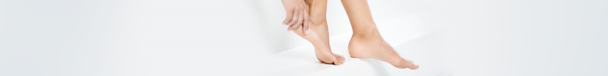 A closeup view of a model touching the heel of their right foot with both feet in view against a white background.
