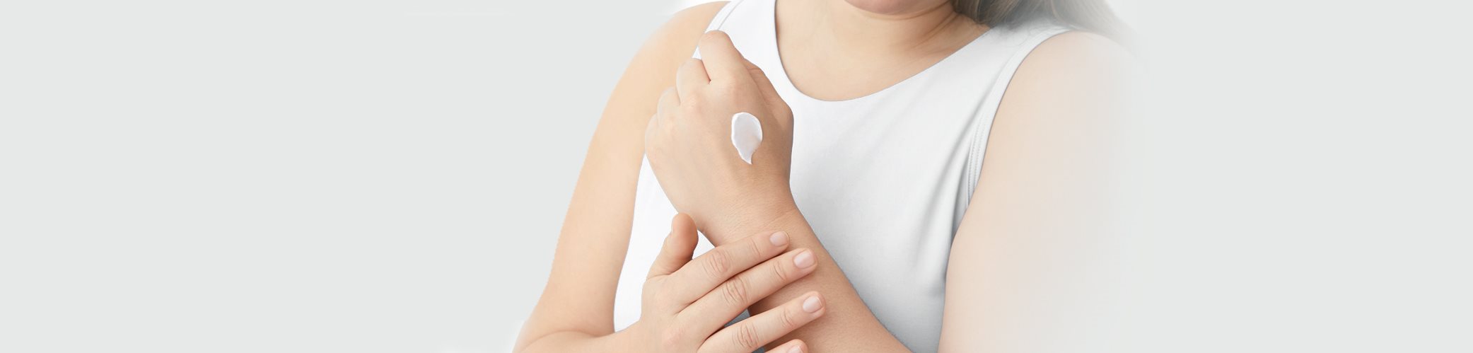 A view of a model wearing a white coloured tank top with Eucerin Eczema Relief cream product smudged on the model's left hand.