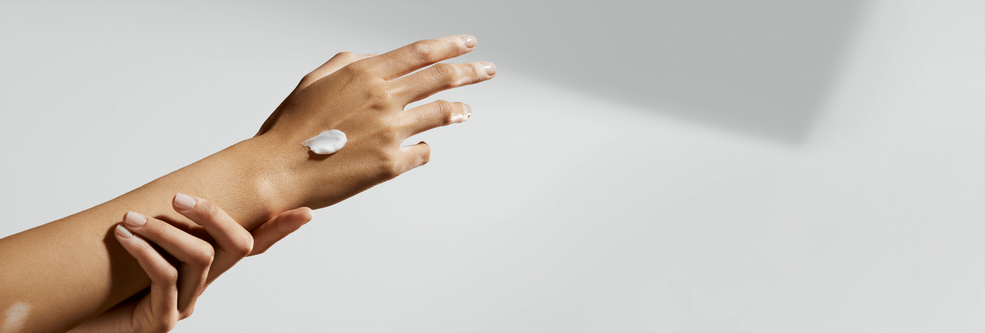Un bras et une main s'étirent, tandis qu'on voit une touche de produit en crème sur la main.