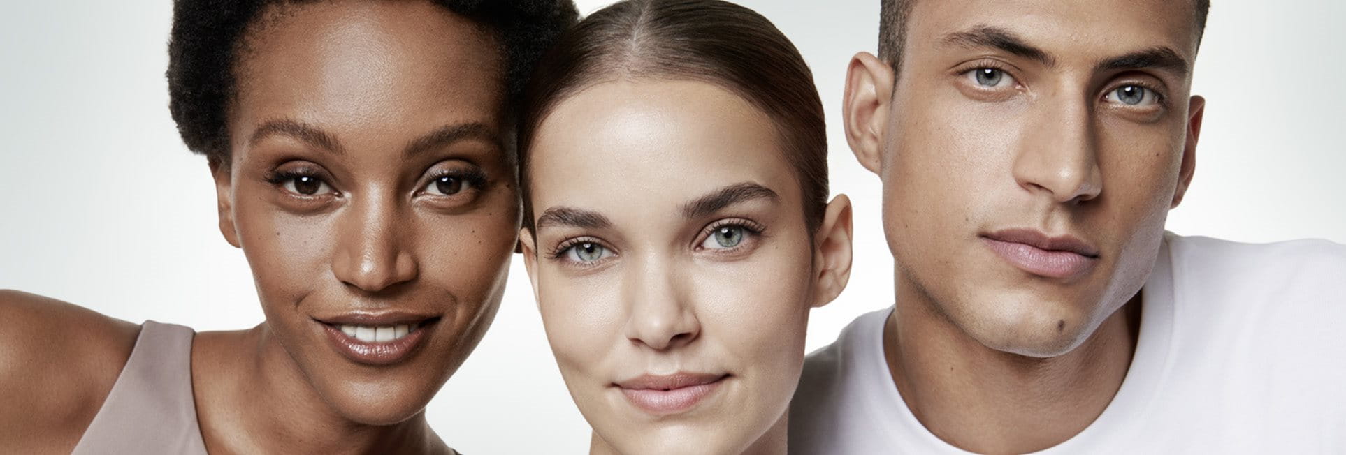 A closeup view of two female models and one male model wearing light coloured tops against a white background.