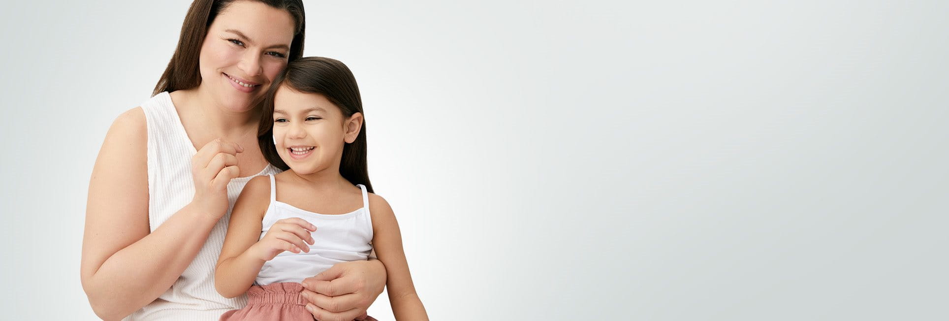 Gros plan d'une femme mannequin et d'une fillette  qui sourient, tandis qu'on voit une touche de  produit en crème sur la joue droite de la fillette.