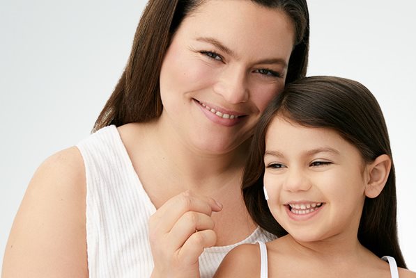 A closeup view of a female model and a little girl smiling with a cream product smudged against her right cheek.