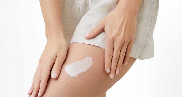 Gros plan d'une femme mannequin portant un short de couleur pâle et montrant du produit en crème étendu sur sa cuisse gauche.
