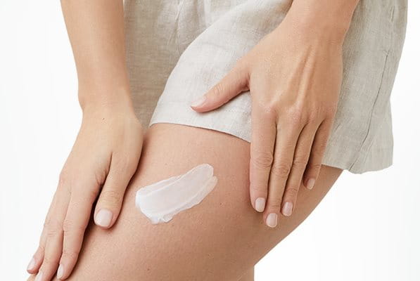 A closeup view of a model wearing light coloured shorts and with a cream product smudged against their left leg.