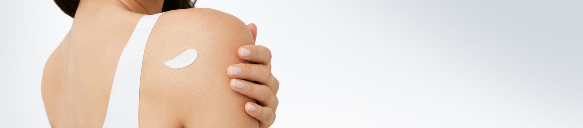 The back view of a model with a cream product smudged against the back of their right shoulder.