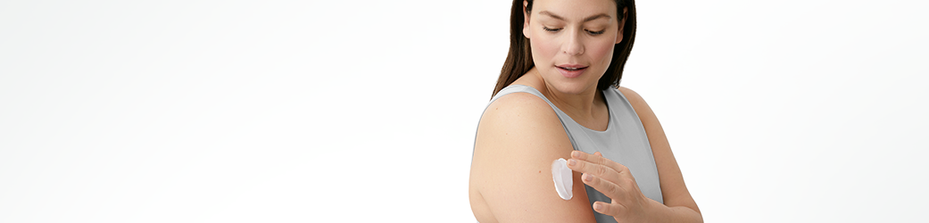 View of a female model with a cream product smudged on her right arm against a white background.