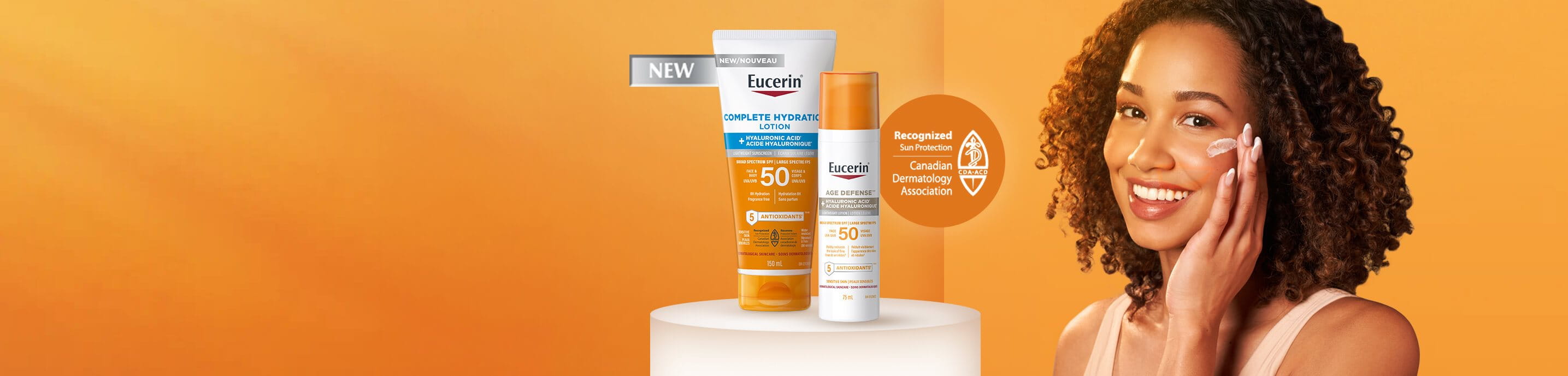 View of a person smiling while applying a Eucerin sunscreen product onto their left cheek, shown against an orange background along with two Eucerin products displayed.