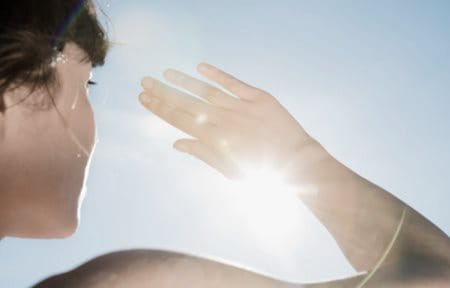 Une femme se protégeant du soleil avec la main.