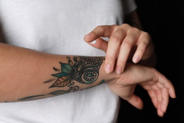 Frau cremt Tattoo am Arm mit Sonnencreme ein