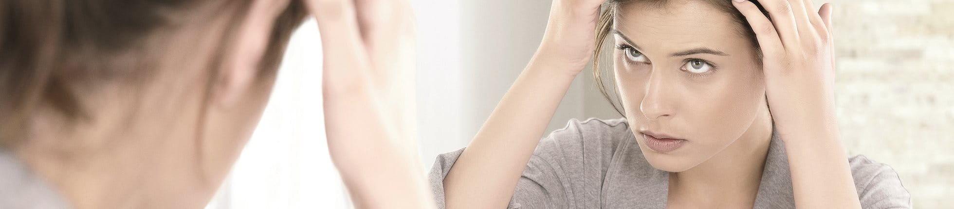 Frau untersucht ihre Kopfhaut am Spiegel