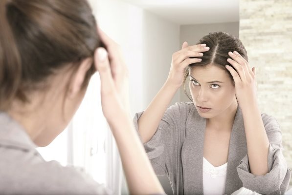 Frau betrachtet Sonnenbrand auf der Kopfhaut im Spiegel
