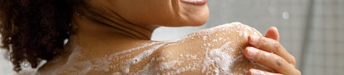 Frau unter der Dusche reinigt Haut auf den Schultern und am Rücken