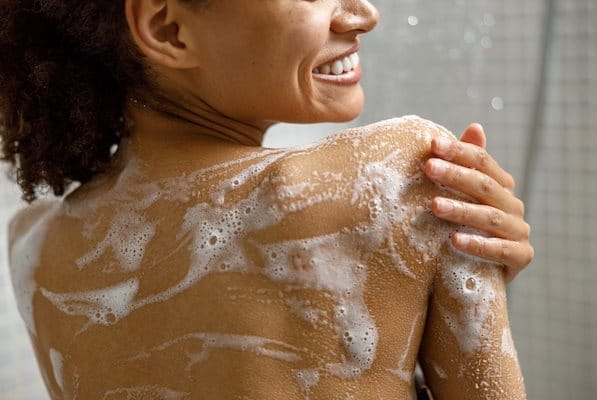 Frau unter der Dusche reinigt Haut auf den Schultern und am Rücken