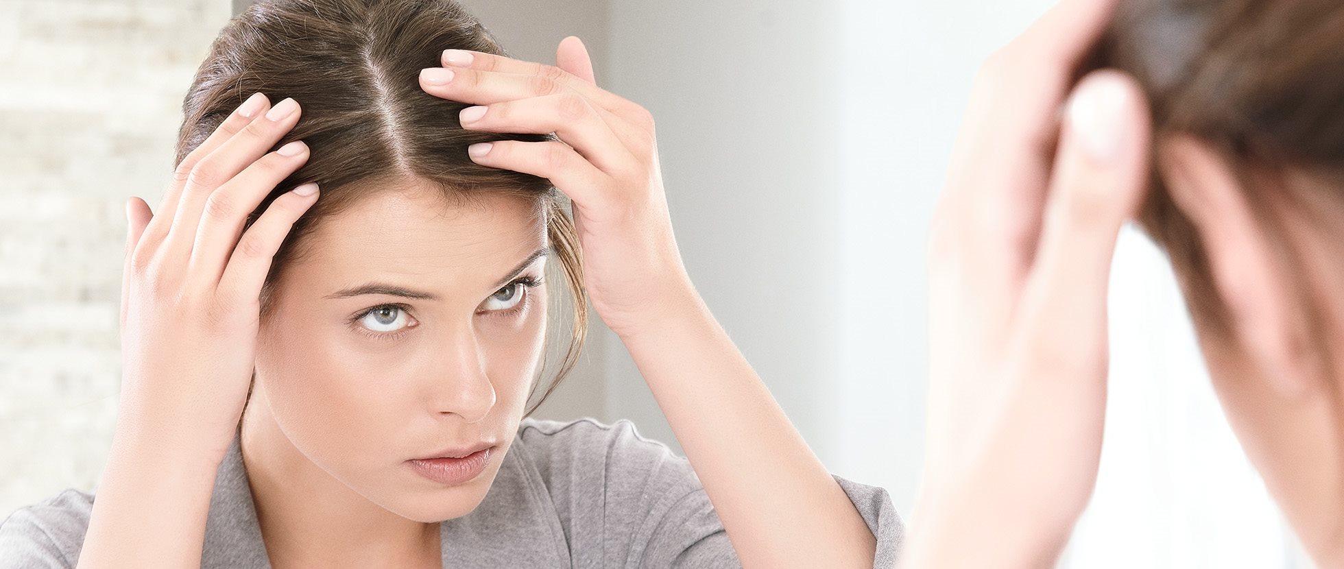 Frau untersucht ihren Scheitel im Spiegel
