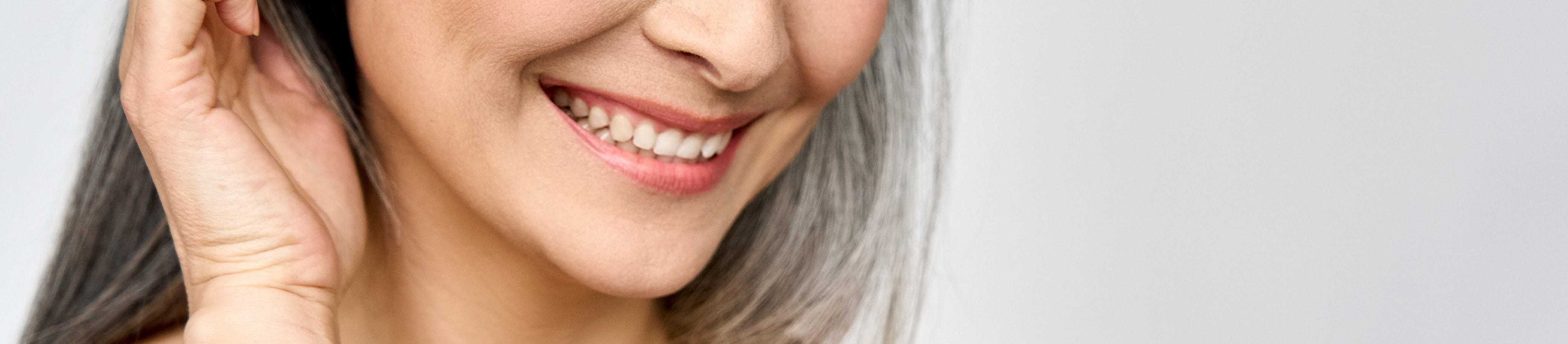 Lachende, ältere Frau streicht sich Haare aus dem Gesicht.