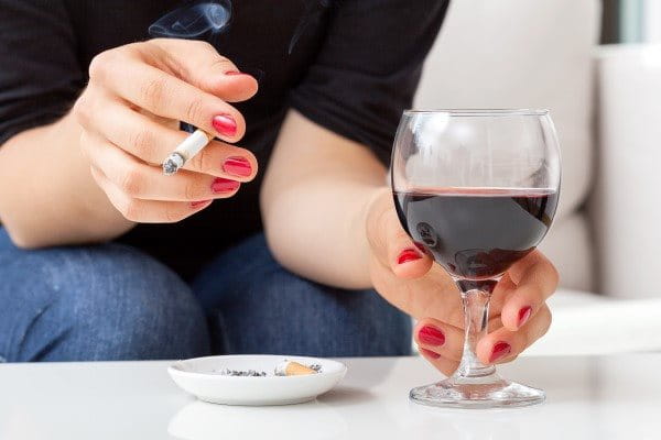  Die Hände einer Frau halten eine brennende Zigarette und ein Glas mit Rotwein.