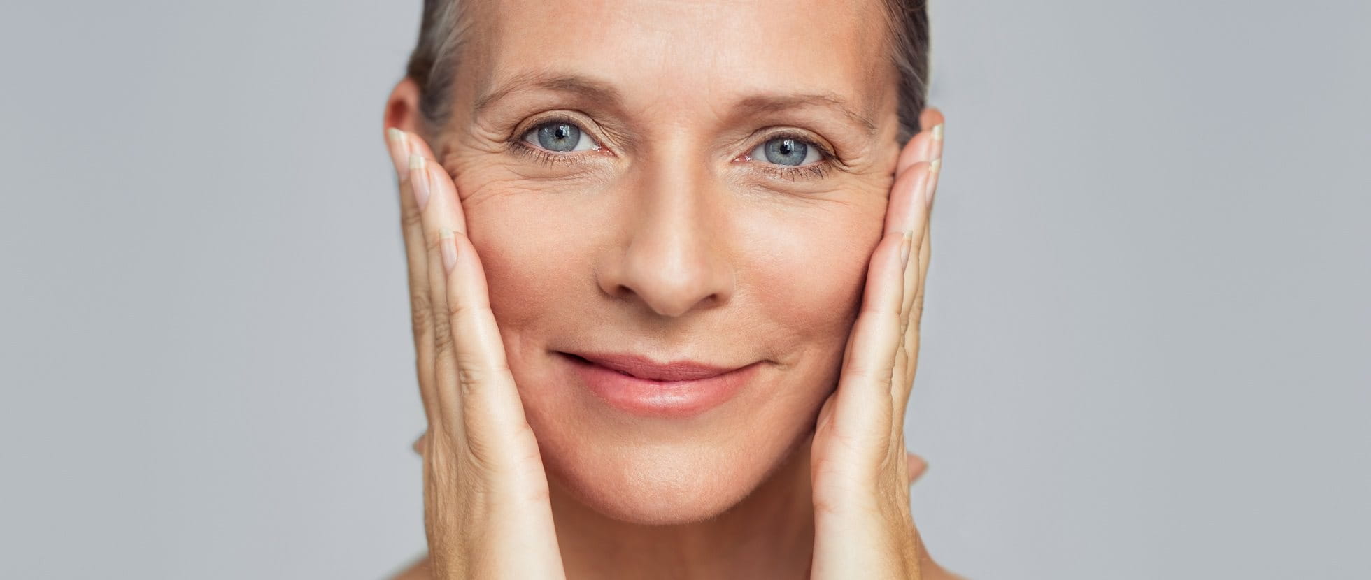 Frau mit Krähenfüßen hält sich die Hände an die Wangen