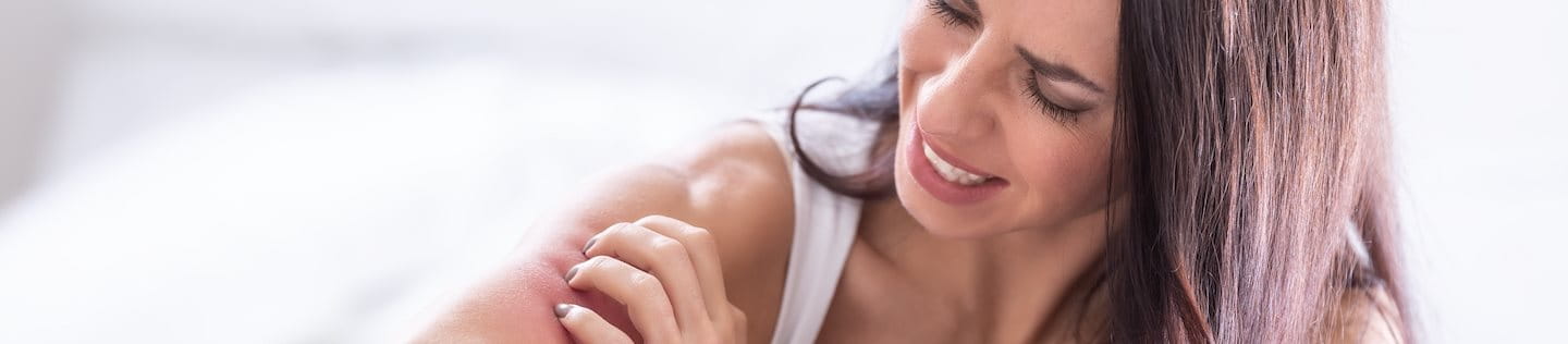 Frau im Bett kratzt sich am Arm