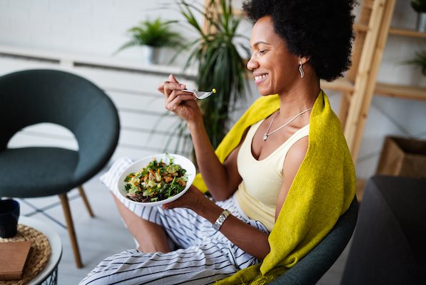 Im Schneidersitz sitzende Frau, die einen gesunden Salat isst