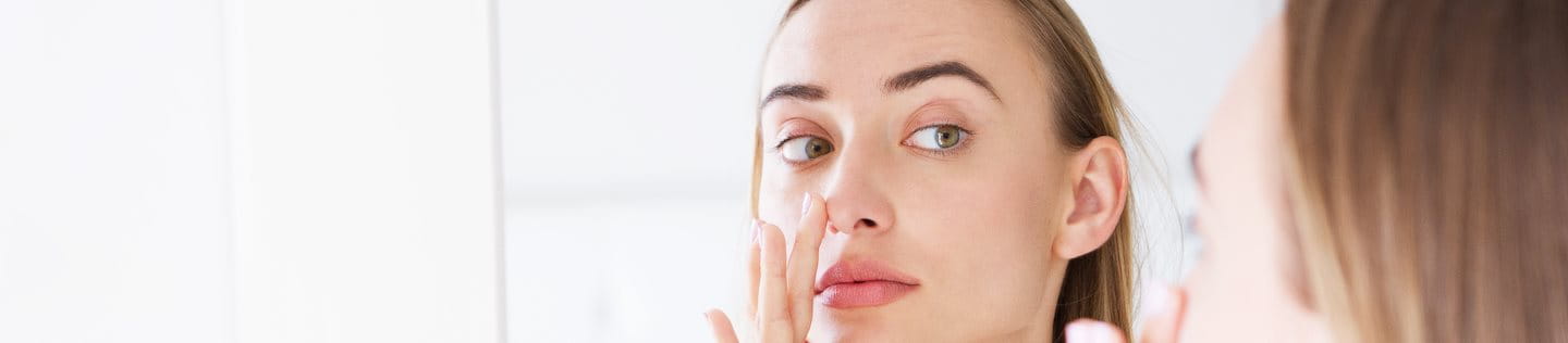 Frau betrachtet Rötung der Nase im Spiegel