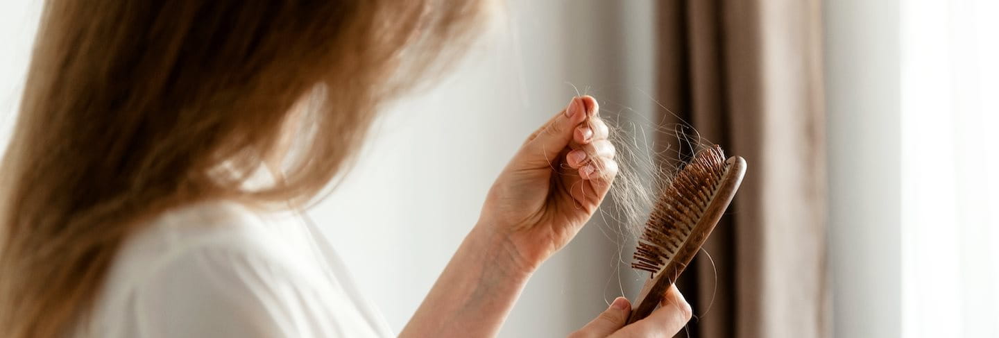 Frau entfernt herausgefallene Haare von einer Haarbürste