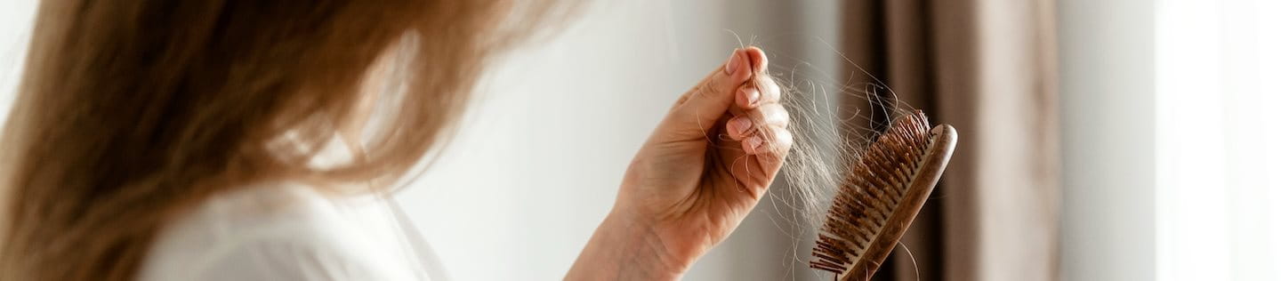 Frau entfernt herausgefallene Haare von einer Haarbürste