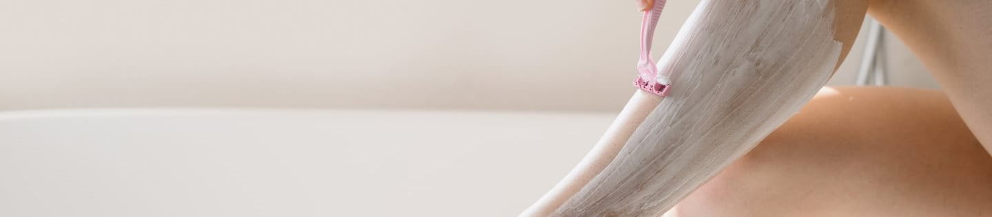 Bein einer Frau beim Rasieren, das auf einem Badewannenrand abgestützt wird.