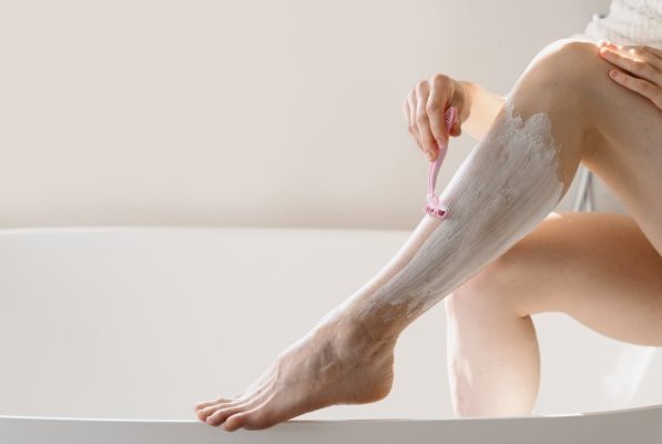 Bein einer Frau beim Rasieren, das auf einem Badewannenrand abgestützt wird.