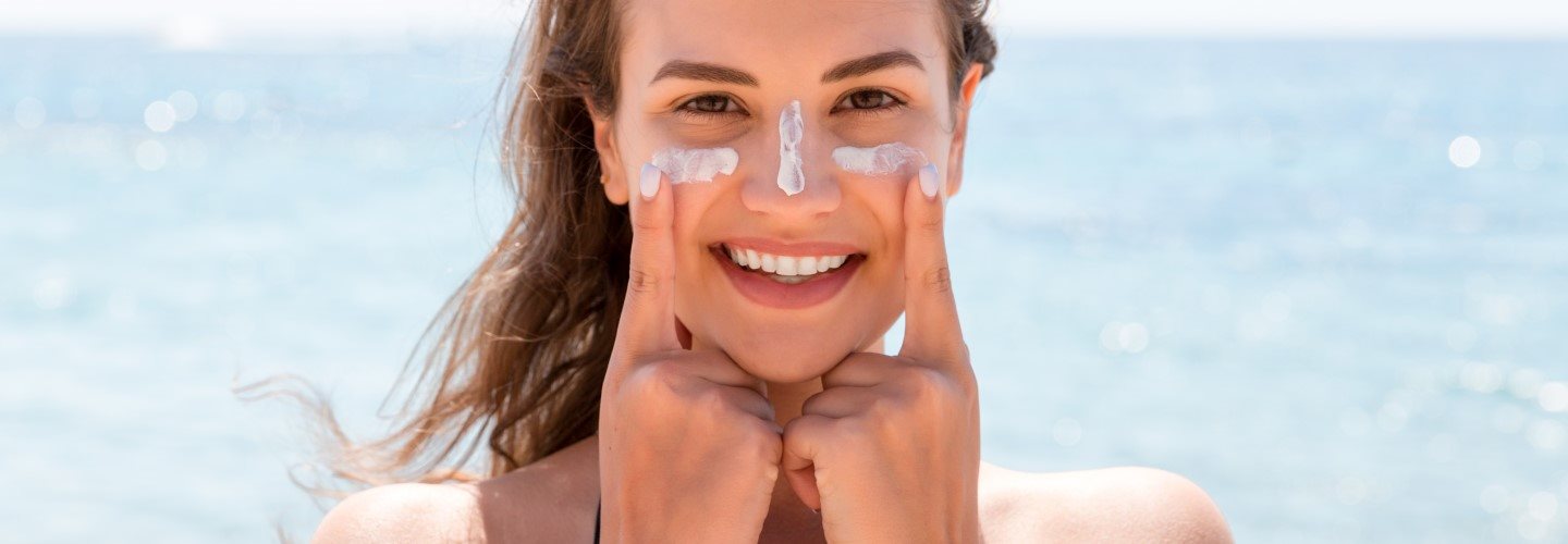 Frau am Meer schützt sich mit Sonnencreme vor Sonnenbrand im Gesicht