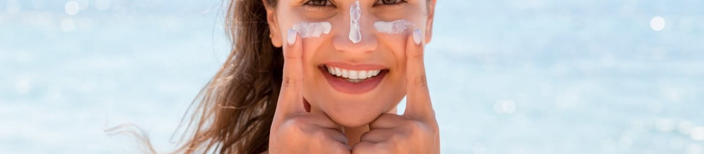 Frau am Meer schützt sich mit Sonnencreme vor Sonnenbrand im Gesicht