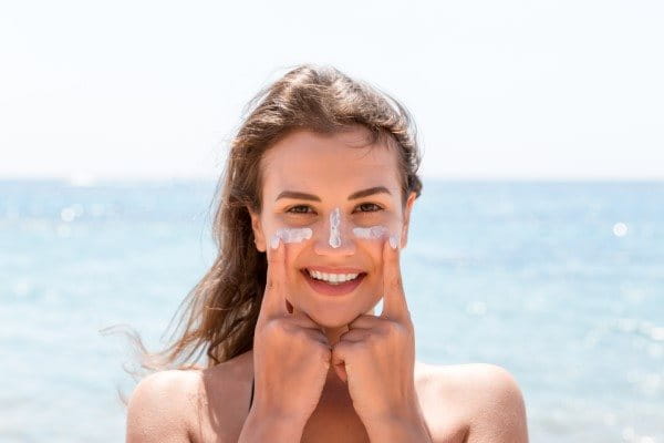 Frau am Meer schützt sich mit Sonnencreme vor Sonnenbrand im Gesicht