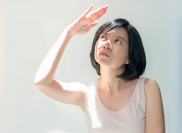 Eine Frau mit hellem Hauttyp hebt ihre Hand zum Schutz vor der Sonne über das Gesicht