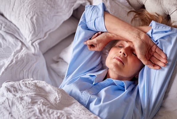 Nahaufnahmen einer Frag mittleren Alters im Bett, mit den Armen auf der Stirn liegend