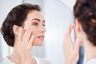 Woman in front of a mirror touching her face