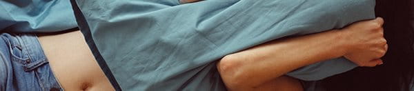 Woman laying in bed covering her face with a pillow