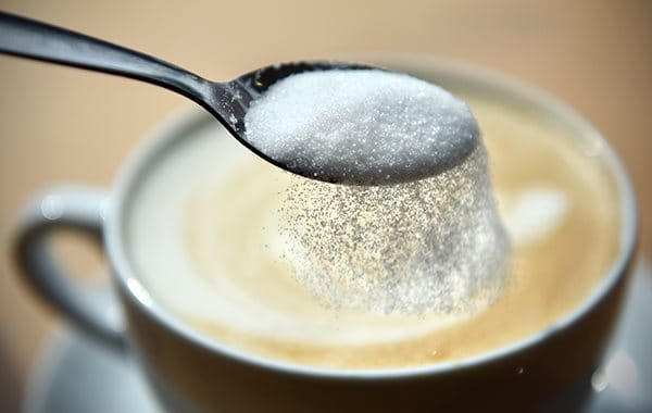 Zucker rieselt vom Teelöffel in den Kaffee