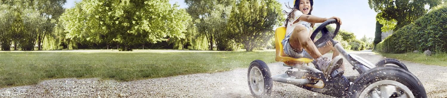 A young girl on a yellow tricycle smiles as she skids across a gravel path