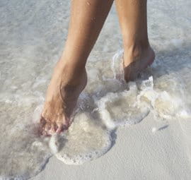 Feet on a beach with incoming waves.