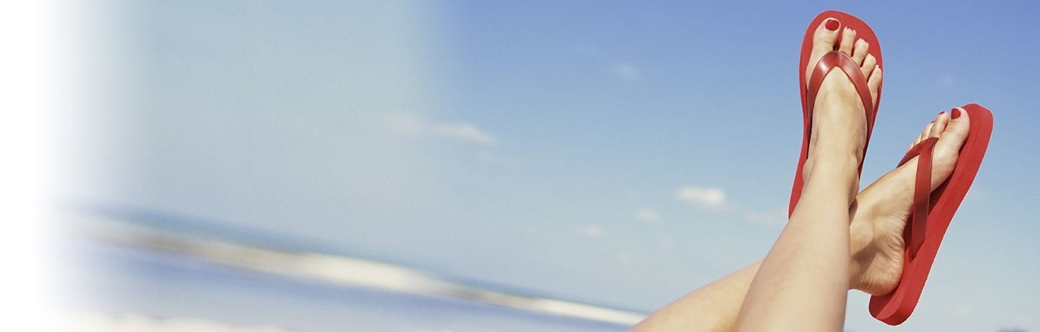 Feet in red flip flops with blue sky in background