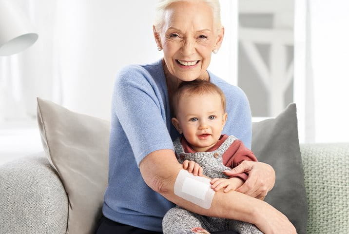 A grandma with a plaster on her sensitive skin is smiling at a baby in her arms