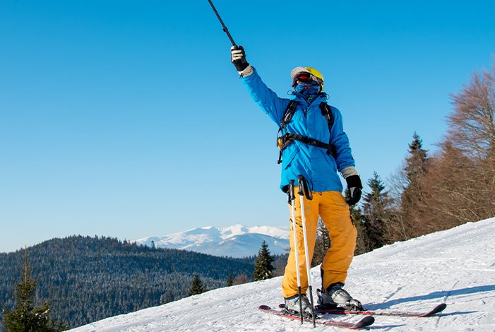 Skifahrer steht auf der schneebedeckten Piste und zeigt mit Skistock in die Luft