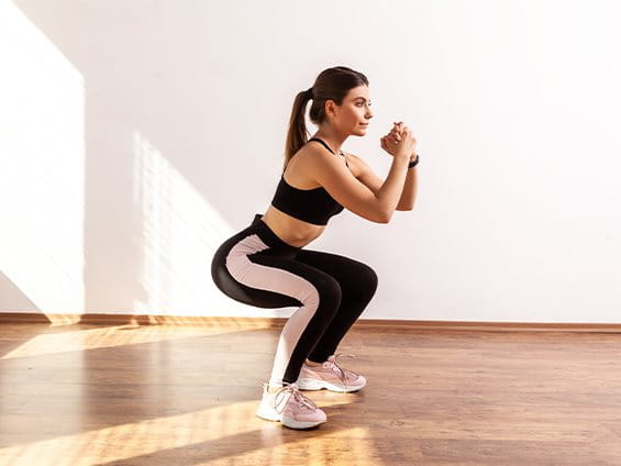 Frau in Leggins und Sport-BH macht eine Hocke