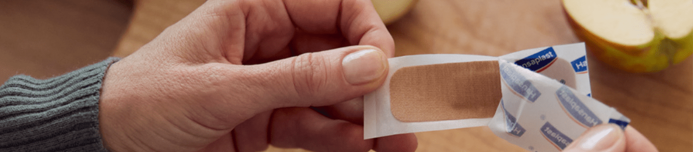 Une personne ouvre un pansement Hansaplast.