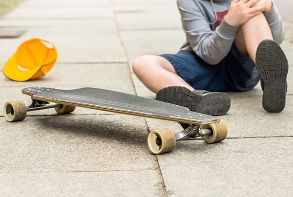Verletztes Kind sitzt neben Skateboard auf dem Gehweg