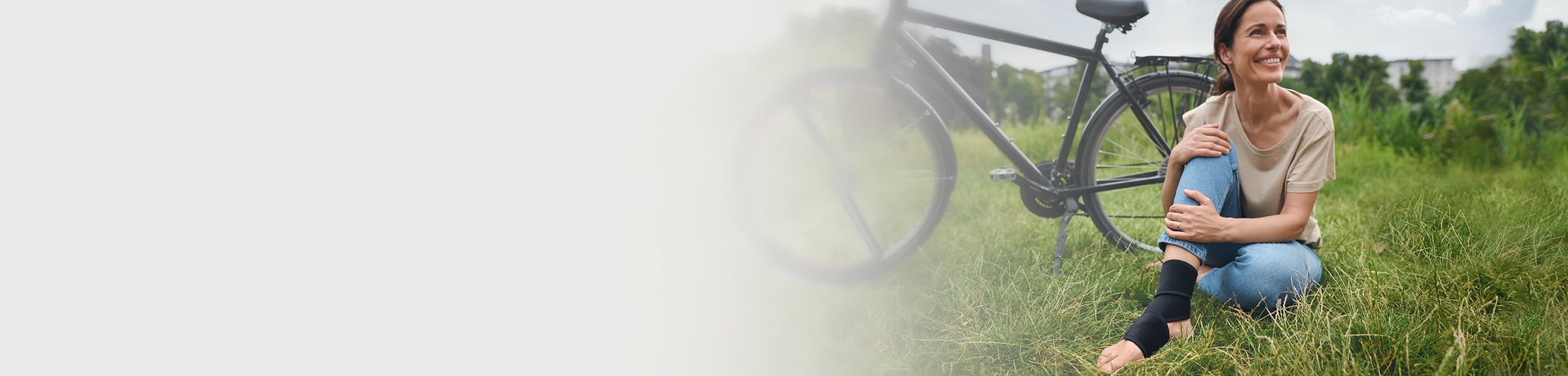Eine Frau, sitzt mit Bandage und Fahrrad auf dem Gras