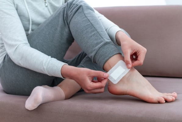 Frau klebt Sensitive Pflaster auf Wunde am Fußknöchel