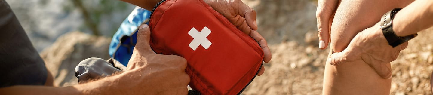 Mann holt Reiseapotheke aus Rucksack für verletztes Knie der Frau