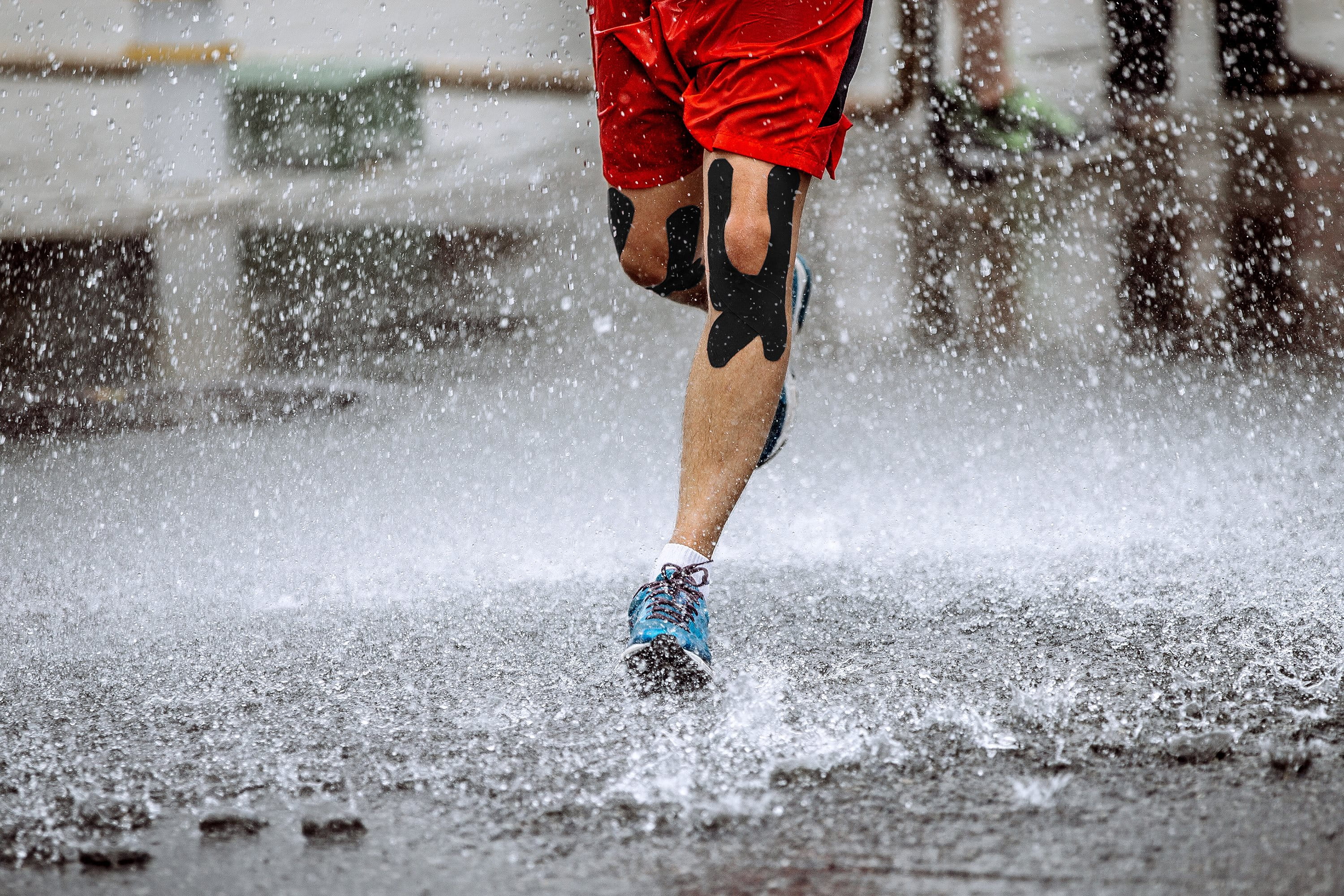 Beine von Jogger im Regen mit getapetem Knie